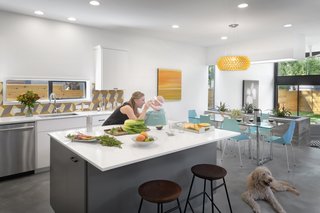 A Mighty Oak Tree Frames This Family Home in Austin - Photo 5 of 10 - In the airy kitchen, meals are prepared on a Silestone White Storm countertop. The backsplash’s tiles match those on the staircase’s risers. In the adjoining dining area, a Caboche suspension light by Foscarini hangs over a CB2 dining table and Real Good Chairs by Blu Dot.