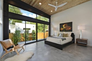 A Mighty Oak Tree Frames This Family Home in Austin - Photo 7 of 10 - The master bedroom looks out at the garden through a full-height glass wall. The Ikea bed sits between Four Hands tables and lies beneath a floral photograph by Stacy Kirk. Opposite the bed, a Jaya chair is situated for quiet contemplation.
