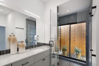 A Mighty Oak Tree Frames This Family Home in Austin - Photo 8 of 10 - Thanks to a sliding glass door in the shower, even the master bathroom manages to retain a connection with nature. Custom cabinetry, a Sielstone Niebla counter and Kohler Verticyl sink, however, all offer compelling reasons to stay inside.