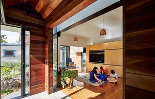 This Transformed Melbourne House Resembles a Quirky Village - Photo 5 of 11 - The owners furnished the living room with a mixture of new and old pieces, including a Hans Wegner lounger and Tuckbox coffee table. A timber-lined hallway leads out from it to the newer parts of the home. Sections of steel-framed double glazing separate and accentuate each "house" while letting in glimpses of sky.