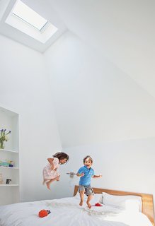 This Farmhouse-Style Home Gets a Clever and Geometric Update - Photo 4 of 5 - Zoe and Jake horse around in their parents’ new master bedroom. Issa says he vaulted the ceiling to fit under the addition’s angular roofline for "spatial impact." Paint is Extra White by Sherwin-Williams.
