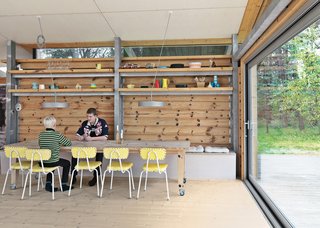 Niels and Jens hang out in the dining area. Like the wall behind it, the table was crafted from the felled trees. The floor is soap-treated pine found offsite. Brask bought the chairs at a flea market; the galvanized-steel pendant lamps are from AART Architects in Denmark. The doors at right open to the deck, which leads to a studio that the boys frequent on their stays.
