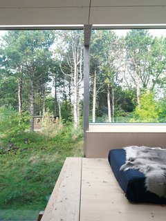 As throughout, steel beams frame a sleeping loft . In the distance is the 100-square-foot trailer Brask brought to the site for the family to occupy during planning and building stages; it is now a guesthouse.