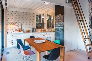 The kitchen is just as detailed and eclectic as the rest of the main floor, with a wall-sized chalkboard and retro wallpaper accenting the streamlined white cabinetry. Bright, colorful dining room chairs add whimsy.