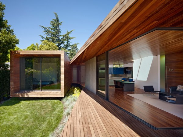 Modern home with living room and medium hardwood floor. The larger volume of the addition, consisting of kitchen, living, and dining spaces, loops around to the smaller bedroom through a wooden passage. The same ipe, with differing finishes, is used for both the interior and exterior. Expansive sliding glass doors by Fleetwood dramatically open up the living space to the outdoors. Photo of 1950s Ranch