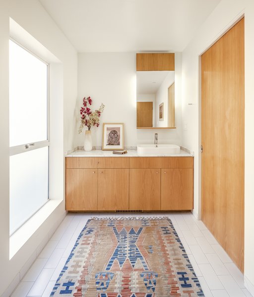 The architect has a track record of stripping away elements of excess to create simple, livable, and well-lit spaces that feel larger than they are. This downstairs bathroom features a simple white ceramic tiles and a sliding white oak door.