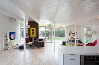 Sunny Renovation of an Eichler Great Room - Photo 1 of 5 - The living spaces of house, built in 1972 or 1973, were originally divided into three—a kitchen, living and dining area, and an atrium (previous owners had covered the atrium with a roof). "The new owners wanted the interior space to flow as one, so we removed the glass doors and solid walls separating the enclosed atrium from the kitchen and living room," principal John Klopf says. "Some structural posts needed to remain to hold up the roof, but overall the space was opened up almost completely. The floor was leveled, and the plan freed up." The rainbow print is a 1960s Herman Miller trade poster, and the Vitamin Water print by a New York artist. A Sapien book tower from Design Within Reach sits next to the TV. The sofa is IKEA.