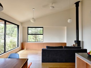 A Breezy Modern Beach House Sits Among the Trees in Australia - Photo 3 of 8 - The homeowners wanted a simple, unfussy space. The walls throughout the home are painted in Dulux Swan White. Built-in cabinets are custom made in Tasmanian oak. The hanging pendants are from About Space and the wood-burning stove is a Morsø 7642 model.