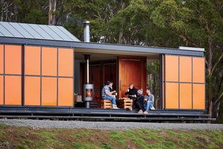 An Off-the-Grid Prefab that Combines Open Plan Living with Rugged Durability - Photo 2 of 10 - The home was designed as a "box within a box," in which two interior structures—an open-plan living space and two en suite bedrooms—sit within its exterior envelope. Inspired by the region’s fiery orange lichen and the indigenous waratah shrub’s bright flowers, the colorful exterior panels are made of heavy-duty galvanized steel to guard from Tasmanian winds, which can reach up to 60 miles per hour.