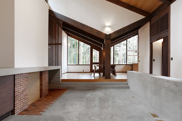 The dining room opens up to the new concrete hearth. Old plans indicate this area was originally intended to be an open courtyard, however, the original clients enclosed it with a leaky glass canopy. The architects installed a new sloped roof that quickly channels away rainfall. The fireplace is composed of brick salvaged from the original floor and the new concrete floor features increased insulation. Photo 6 of Zema Redux modern home