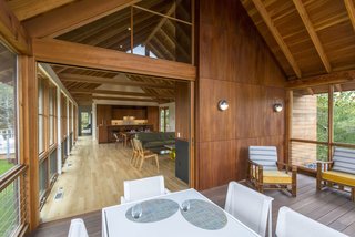 In a Cape Cod retreat, a sliding door opens to a relaxed screened-in porch. Varying types of wood make up the home's interior: white oak planks for the floor, solid mahogany for the cabinets, and fir for the ceilings, beams, columns, and trim.