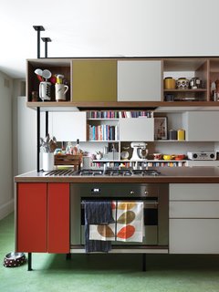 Kitchen Confidential <br><br>Kiely and architect Maxim Laroussi designed the kitchen unit. "I originally didn’t want an island, but I liked what we did because it feels like a piece of furniture. It’s cozy to cook around," Kiely says. Panels of orange and olive Formica accent the 1950s-inspired piece, which houses a cooktop by Smeg. A checkerboard of closed cabinets and open shelves offers storage against the far wall for Kiely’s collection of dishes, knickknacks, cookbooks, and small appliances, like the KitchenAid stand mixer and radio by Vita Audio. The floor is green Marmoleum, selected because it feels warm underfoot. Kiely’s own Stem dish towels and ceramic storage jars add more lively color to the room.