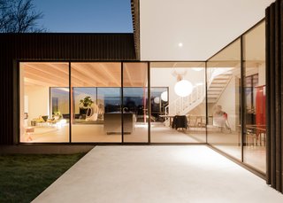 This Blackened Timber House Triumphantly Emerges After a Fire - Photo 3 of 6 - The entrance has a simple white ceiling, the dining table sits in a double-height space, and the living room has a warm spruce ceiling, subtly dividing the open floor plan. The interior flooring (a custom mixed shade of Invedra concrete) was also used on the patios, which help facilitate the indoor-outdoor cohesion.
