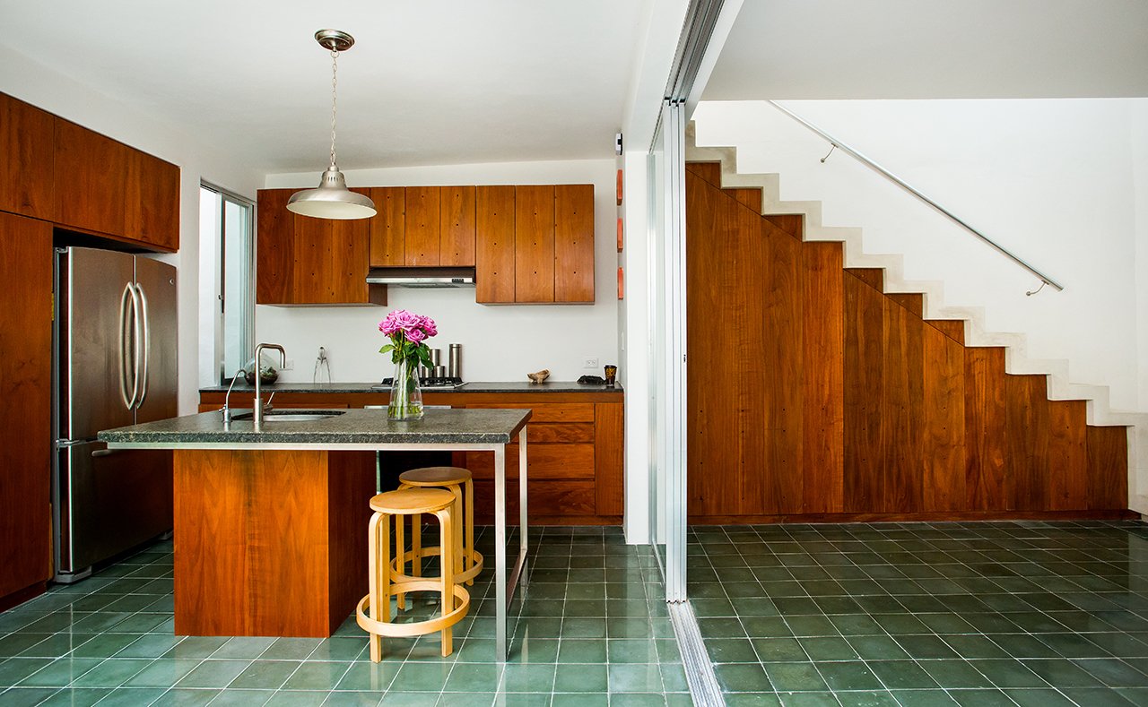 Handcrafted green cement tile floors are used in the kitchen and in many living spaces in the home. Honed granite counters, Tzalam wood cabinets, and GE Profile appliances complete the airy space.