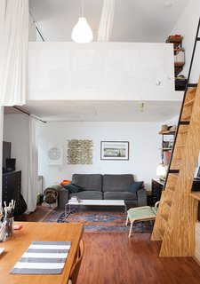 The living room is tucked beneath one of the lofts, which are accessible by a steep ladder-like staircase and fronted by pegboard.