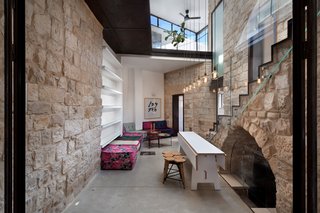 A 250-Year-Old Stone House in Israel With a Surprisingly Modern Interior - Photo 4 of 7 - Warm and casual furniture is favored in the courtyard. Colorful seating, wood stools, and smart built-in shelving complete the space. The expandable table by Henkin Shavit is flanked by seven hanging pendant lights, symbolizing the branches of the Menorah. To the right of the table, the original stone arch leads to the home’s wine cellar.