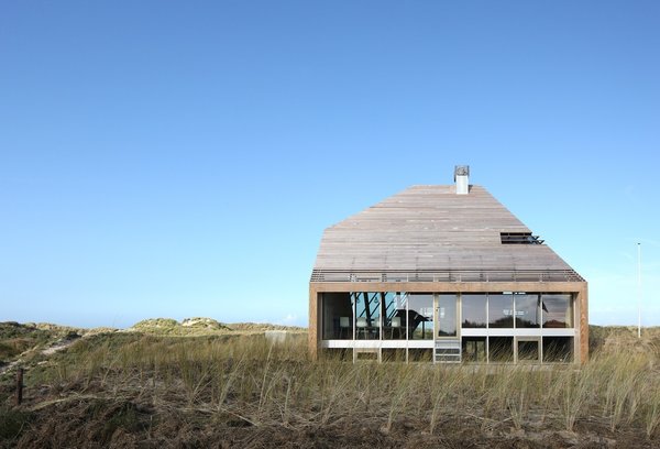 The home, a half-sunk diamond, is experienced very differently from each of its sides. Using BIM software, the firm designed modular prefabricated wooden panels that make up each of the home’s facades. Western red cedar was chosen for the panels, while tropical Bilinga was selected for the edge beam. Photo of Dune House modern home