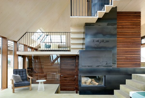 The interior staircase spirals around the center of the home, in a “promenade architecturale” connecting each level. The continuous and gradual vertical movement is a subtle nod to the experience of strolling through the dunes. A central wood-burning fireplace efficiently heats the whole home, minimizing the need for supplemental in-floor heating incorporated in the concrete floors. Natural cross-ventilation is achieved through the use of CO2 directed grills at the north and south of the home, an added green feature that further reduces the ecological footprint. Photo 5 of Dune House modern home