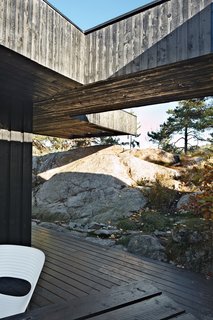 30 All-Black Exterior Modern Homes - Photo 17 of 30 - A section of the roof reaches over a rock outcropping—a detail that visually connects the house to the landscape and offers a handy way to climb up to the roof deck without using a ladder.
