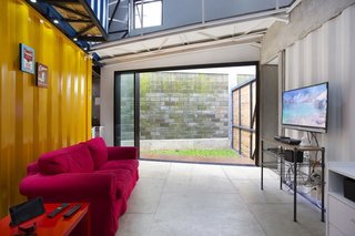How to Stay Cool by Living in a Shipping Container - Photo 7 of 10 - A sliding glass door in the downstairs living room leads to an outdoor patio and green space. A sofa and side table from IKEA complement an unfinished wood entertainment center.