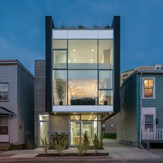The Architect Next Door - Photo 1 of 9 - The home’s front façade features an anodized aluminum and glass curtain wall by Kawneer that's framed by Vic West black corrugated metal panels. The board-formed concrete on the exterior enables passive solar absorption, allowing optimal heat retention on cold winter days. The metal and concrete exterior cladding offers cohesive dialogue with the neighboring industrial sheds and commercial buildings.