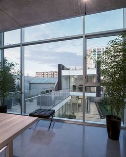 The Architect Next Door - Photo 2 of 9 - The main living area is connected to the back unit by a modern bridge. Polished concrete is used for both floors and ceilings, and a Mies van der Rohe Barcelona Stool accents the space.