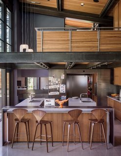 A Forest Sanctuary Designed to Support Autistic Triplets, Their Parents, and a Host of Caregivers - Photo 8 of 19 - Norman Cherner barstools from Design Within Reach line the island in the kitchen, which is crowned by an open loft office. The faucets are from Dornbracht; the countertops are Caesarstone. Hawkins integrated a steel-clad casual eating nook, at left.