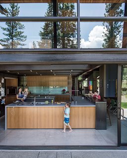 A Forest Sanctuary Designed to Support Autistic Triplets, Their Parents, and a Host of Caregivers - Photo 12 of 19 - The kitchen opens to the elements thanks to sliding doors from C.R. Laurence. The anigre in the kitchen is the same employed in the master bedroom.
