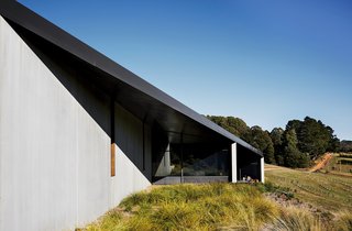 Richly Furnished Home Frames Striking Landscape Views - Photo 1 of 10 - Embedded in the rugged southern Australian landscape, the House at Hanging Rock comprises three volumes connected by a sweeping rhomboid roof. The Colorbond steel overhang is in a dark-gray shade called Monument.