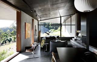 Richly Furnished Home Frames Striking Landscape Views - Photo 9 of 10 - The interior shares the structure’s attention to texture and line. Furnishings include a pair of Arne Jacobsen’s AJ floor lamps and a Le Bambole sofa, armchairs, and ottoman by Mario Bellini for B&B Italia.