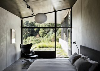 Richly Furnished Home Frames Striking Landscape Views - Photo 6 of 10 - The master bedroom, which features a bed by Paolo Piva, an Egg chair by Arne Jacobsen, and a Ball pendant lamp by George Nelson, opens directly onto a verdant patio. The metal shutters at the bottom of the window keep out flying embers in case of fire.