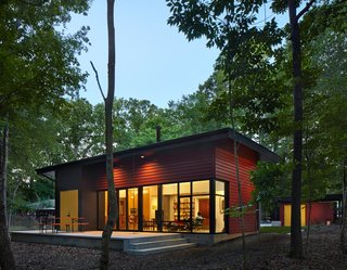 This Light-Filled, Metallic Home Embraces Its Wooded Site - Photo 1 of 8 - Nestled in a forest, the residence consists of three volumes. The patio, enhanced by a German-made beer garden table, is an extension of the living room floor, creating an indoor-outdoor living space. "It’s one way a small space can be made to feel larger," says architect Jason W. Hart. All of the exterior doors are painted marigold, providing a friendly pop of color.