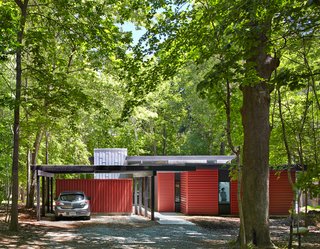 This Light-Filled, Metallic Home Embraces Its Wooded Site - Photo 2 of 8 - Topped with translucent polycarbonate roof panels, the carport and storage shed helps buffer the home from the road. "It’s part of easing into the site with increasing enclosure along the entry axis," Hart says. "We created a purposefully drawn-out experience that’s intended to heighten awareness of the site and gradually transition from the forest to the home."