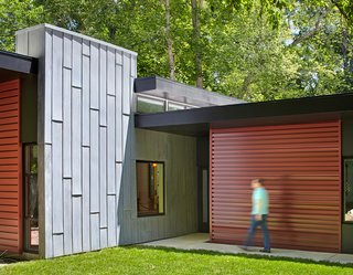 This Light-Filled, Metallic Home Embraces Its Wooded Site - Photo 4 of 8 - A tall gray wall, made of acid-washed zinc metal, marks the entryway and visually grounds the roof planes. It also separates the living and bedroom volumes.