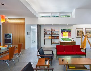 This Light-Filled, Metallic Home Embraces Its Wooded Site - Photo 5 of 8 - The Aiyyers’ midcentury furniture collection adds personality and color to the open-plan interior. A sofa by Kofod-Larsen for Selig, chairs by Viko Baumritter, shelving by Regner Christensen, and a coffee table by a local craftsmen accentuate the living room, while a dining table and chairs by Calligaris, custom cabinetry with pulls by Mockett, and an overhead Bel Occhio light from Pablo Designs complete the kitchen. Leigh’s harp, from Lyon & Healy, sits nearby.