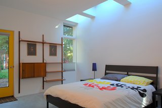 This Light-Filled, Metallic Home Embraces Its Wooded Site - Photo 8 of 8 - In the bedroom, an IKEA bed frame and CADO wall unit are drenched with natural light during the day from the skylights overhead. "The effect of daylight through skylights is very different than from a window," Hart says. "You feel every minute of the day as light in the space ebbs and flows with the passing clouds."
