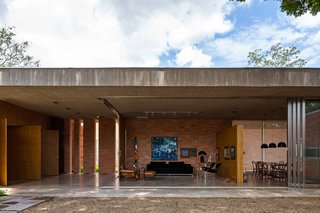 This Cor-Ten House in Brazil Would Not Be Complete Without its Giant Home Library - Photo 5 of 7 - The home’s living room can be kept open to the elements, or sectioned off with sliding glass walls. A natural concrete slab acts as an exterior barrier, and freijó wood and track lighting define the interior space. C10 sofa by Marcus Ferreira and vintage Poltrona Molé chair by Sergio Rodrigues provide casual seating. Across the partition wall, a Jader Almeida table anchors the dining room.