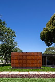 This Cor-Ten House in Brazil Would Not Be Complete Without its Giant Home Library - Photo 1 of 7 - The geometric front facade of the home is made of Cor-Ten steel, segregated into eight vertical panels. Juxtaposed with its lush natural environment, the front elevation is a minimal and abstract counterpoint to its surroundings. An exterior pool meets the facade at its base.