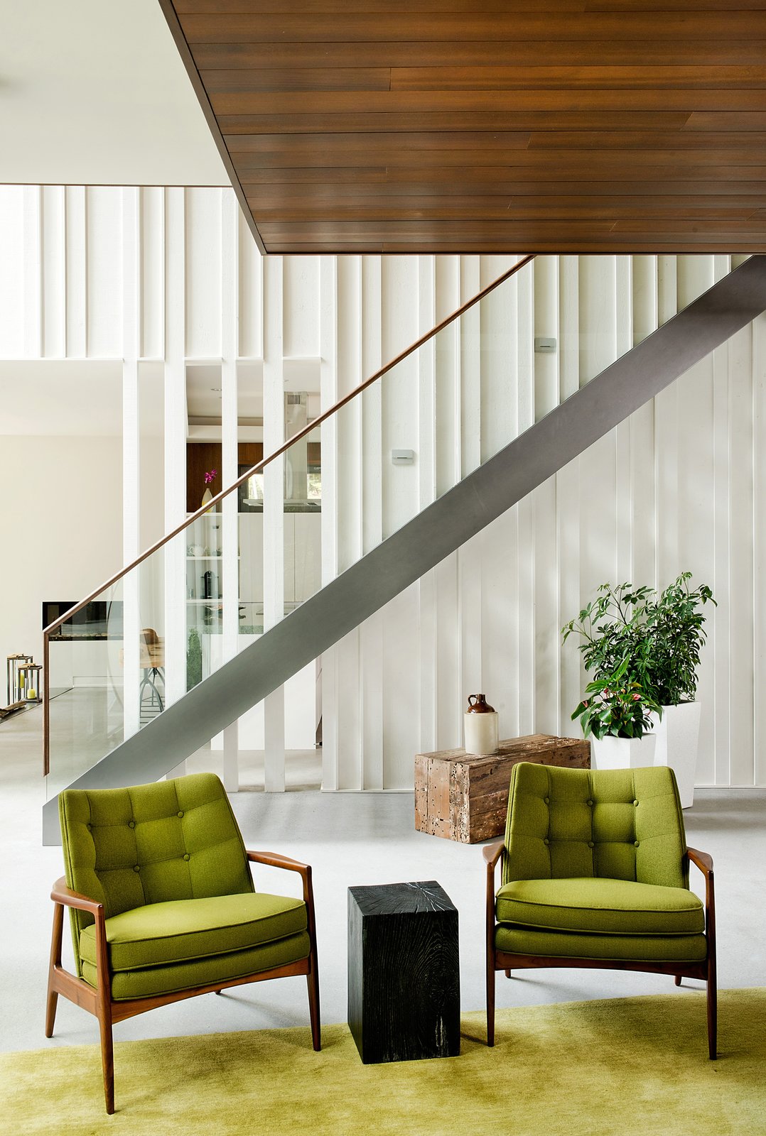 Raw wood planks were painted white and fitted next to a staircase and banister by Bättig Design. Matching chairs by Thayer Coggin sit atop a Crate and Barrel rug.
