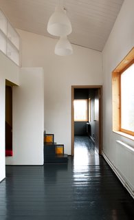 A Compact Home in Moscow Built on the Lowest Possible Budget - Photo 4 of 9 - A pair of lights from IKEA hang above the first floor, which houses the living room, kitchen, and bathroom. Pine floors, painted black, run throughout the residence.
