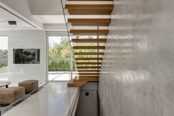 Inside, the home immediately opens up with light and natural views. The cantilevered stairs leading to the first floor offer a dramatic focal point. The stairs, wrapped in natural oak, are anchored to the exposed concrete walls on one side, and bordered by a clear glass railing on the opposite side. Photo 2 of Rishon Le Zion 3 modern home