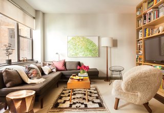 This Luxurious Apartment in Greenwich Village Is Only 520 Square Feet - Photo 3 of 6 - Along with a Dunbar sofa covered in Romo fabric, occasional seating includes a sheepskin Finn Juhl Pelican chair and a vintage wire chair. A BDDW coffee table sits atop a vintage rug. The artwork is by William Steiger.
