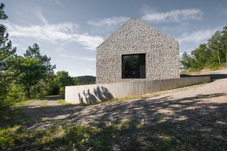 Resembling its neighbors, the pitched form of the Compact Karst House is made of a mixture of local limestone and concrete, cast on site. A small perimeter wall in reinforced concrete surrounds the structure.