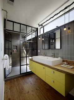 In the bathroom, a teak live-edge countertop and custom yellow cabinet support a double wash basin by Duravit. A mirror from Restoration Hardware hangs below custom lights, designed by the homeowner for a steampunk look.