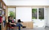 Modern home with living room and concrete floor. Averse to the idea of a television being the centerpiece of a space, the owners instead opted for a clever alternative in the library/media room. Continuing the theme of movable and multi-functional design elements, a rolling chalkboard panel was designed to conceal the TV when not in use. Throughout the home, the family’s furniture is an eclectic mix of purchased, custom built, inherited, and self-made pieces. The room is accented with a reclaimed red office chair with custom white oak armrests made by Scholz. Photo 3 of KS Mission