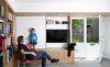 The sliding wall panel is seen in its open position. In addition to several design elements serving multiple functions, great care was taken to develop a compelling design within the constraints of existing conditions. The remodel was confined to the existing building envelope, leaving the original footprint unchanged, but adding about 650 square feet of habitable space in the process. “The plans,” explains Paré-Mayer, “respected existing structural conditions where possible to save on cost.” The finished concrete floor is, in fact, the structural slab, an efficient choice from a cost and materials perspective. The existing footings, which were wider than the framed interior walls, were kept intact in their original condition and location. The team was able to cleverly design around them by building usable closed storage to conceal the protruding foundation, as seen at the base of the media built-in. Photo 4 of KS Mission modern home