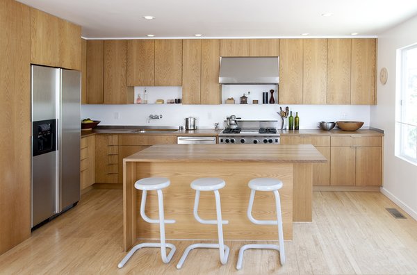 The kitchen was given an economical revamp by adding new drawer and door fronts to the existing cabinet boxes. Countertops were replaced with custom fabricated white oak butcher block surfaces, and a complementary white oak kitchen island was installed. A Wolf range, Vent-a-Hood hood, Franke stainless steel sink, and Bosch dishwasher complete the space. Photo 8 of KS Mission modern home