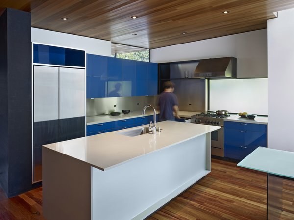 Modern home with kitchen, colorful cabinet, medium hardwood floor, metal backsplashe, engineered quartz counter, ceiling lighting, range, refrigerator, and undermount sink. Accenting the warm wood tones, pops of cobalt blue are found throughout the home, including in the kitchen. The space, which anchors the new living wing, features custom lacquer finish cabinets, Caesarstone counters, a Bertazzoni range, a Miele dishwasher, a Kohler sink, and a custom stainless steel backsplash. Photo 4 of 1950s Ranch