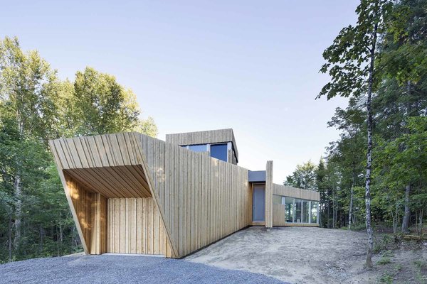 Locally sourced white cedar camouflages the home’s exterior. Bernier and his team installed weatherproofing behind the vertical wood panels, which vary in width and thickness, as a means to hide the molding and trim that are usually visible on traditional wood structures. From a distance, the home looks like a palisade that follows the shape of the terrain. Photo 3 of House of Lake Grenier modern home