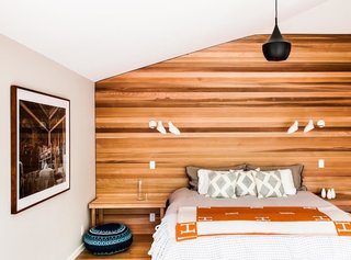 The master bedroom of this East Hampton vacation home features a single wall of textured Western red cedar and lighting by David Weeks Studio. "We brought the cedar siding of the exterior inside strategically, both to blur inside and out and to give texture," Young says. "Simple forms and clean lines, if done right, have a calming effect and nicely contrast the furnishings."